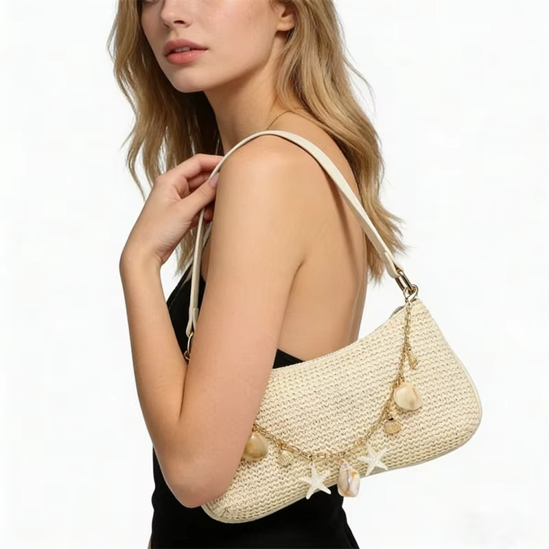 Sac en paille baguette beige avec bandoulière et chaînette ornée de breloques coquillages porté sur l'épaule