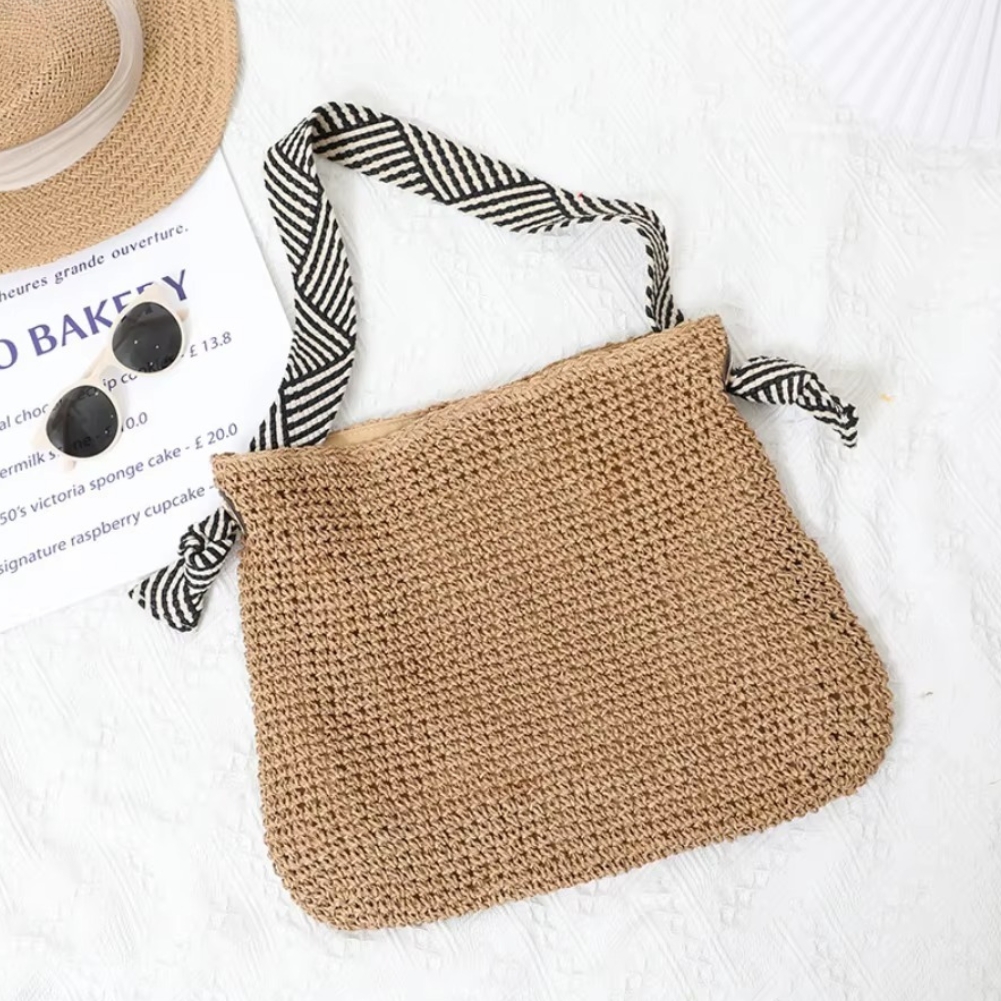 Sac en paille crochet avec bandoulière rayée noire et blanche modèle Bertille posé sur un tissu blanc