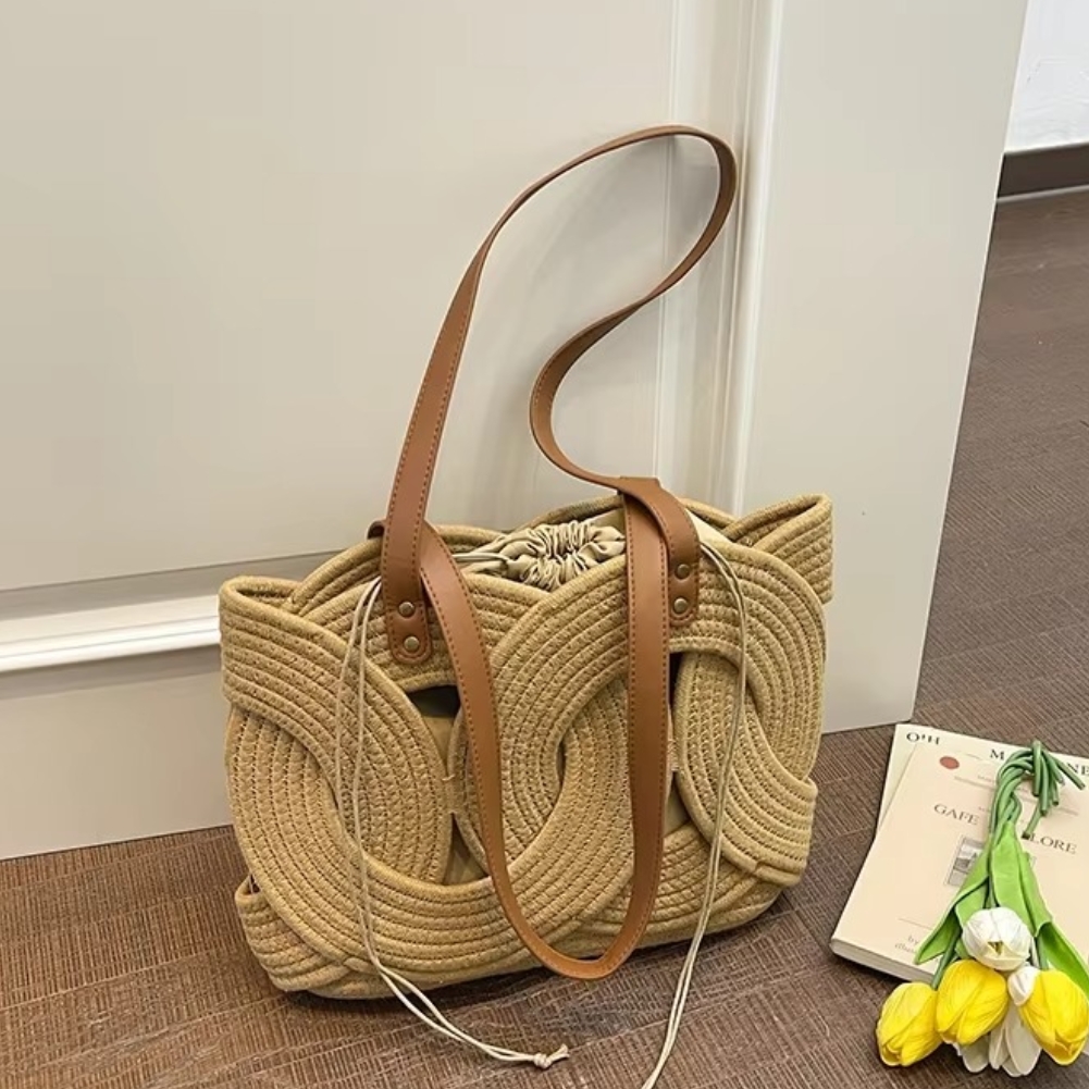 Sac en paille crochet couleur naturelle avec motif feuilles et anses en cuir marron modèle Elodie posé sur un sol à côté de tulipes jaunes et d'un livre