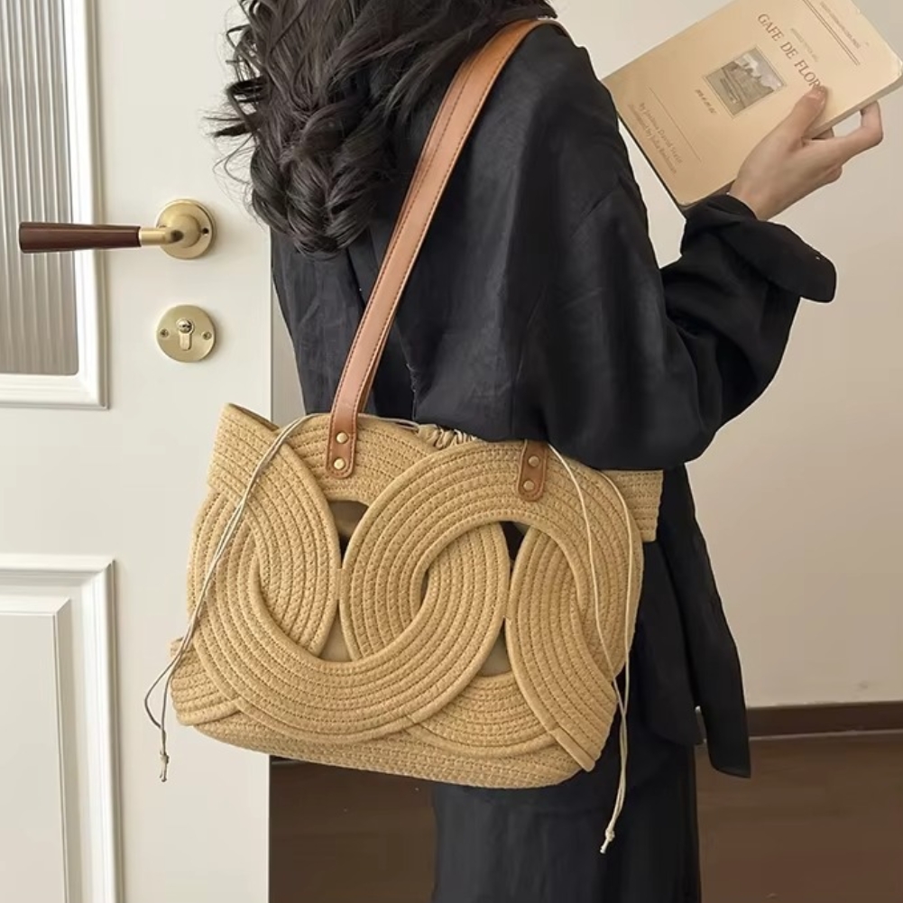 Sac en paille crochet couleur naturelle avec motif feuilles en relief porté à l'épaule par une personne habillée en noir