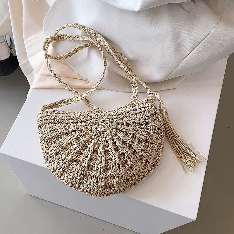 Sac en paille demi-cercle couleur naturelle avec pompon et bandoulière tressée modèle Amandine posé sur un support blanc