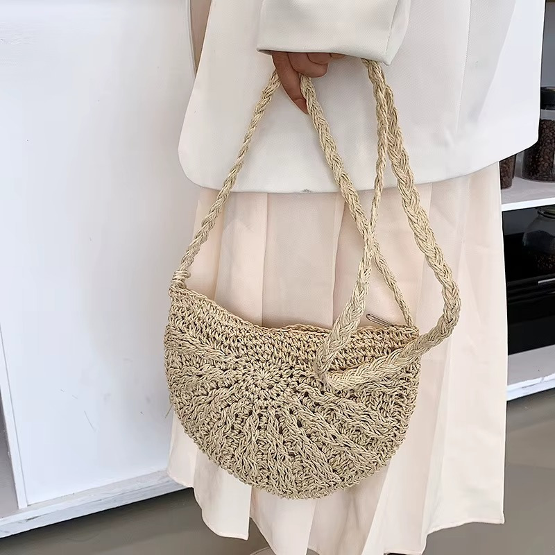 Sac en paille demi-cercle avec pompon et bandoulière tressée porté à la main