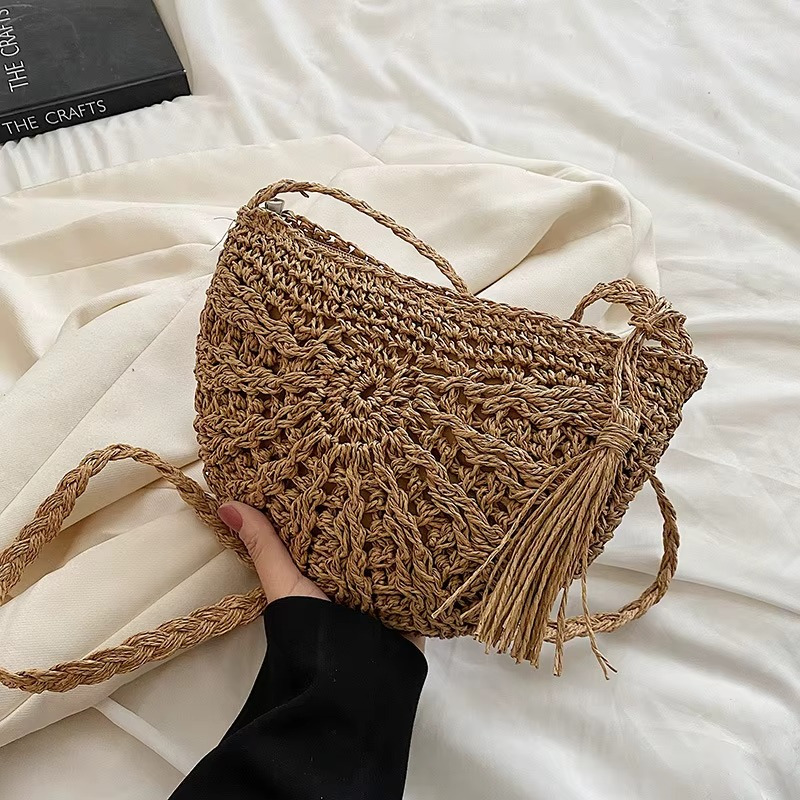 Sac en paille demi-cercle avec pompon et bandoulière tressée modèle Amandine porté à la main sur fond clair