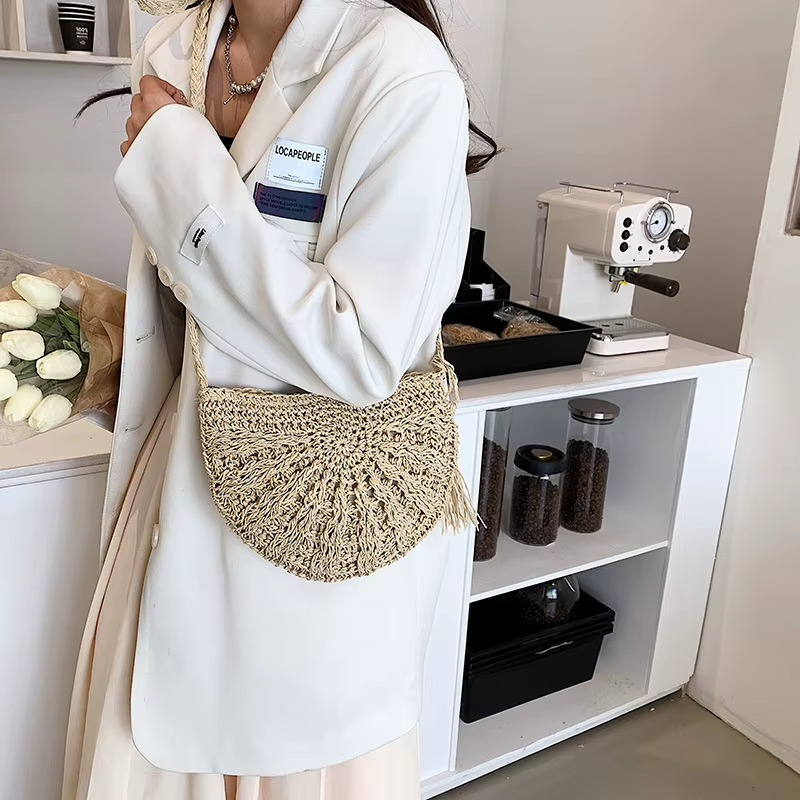 Sac en paille demi-cercle avec pompon et bandoulière porté en travers sur une veste blanche