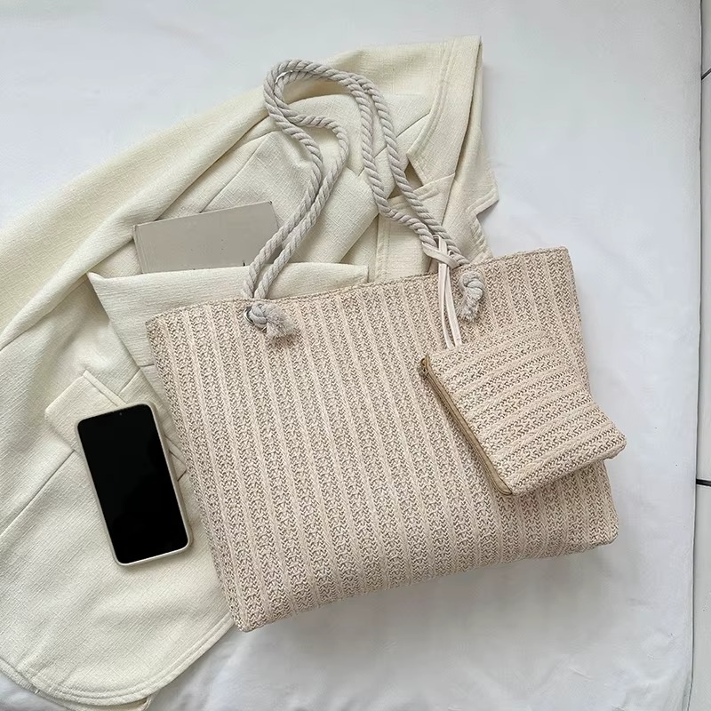 Sac En Paille Grand Format Fourre-Tout – Juliette Sac en paille grand format fourre-tout Juliette beige avec poignées en corde et petite pochette assortie posés sur un vêtement clair