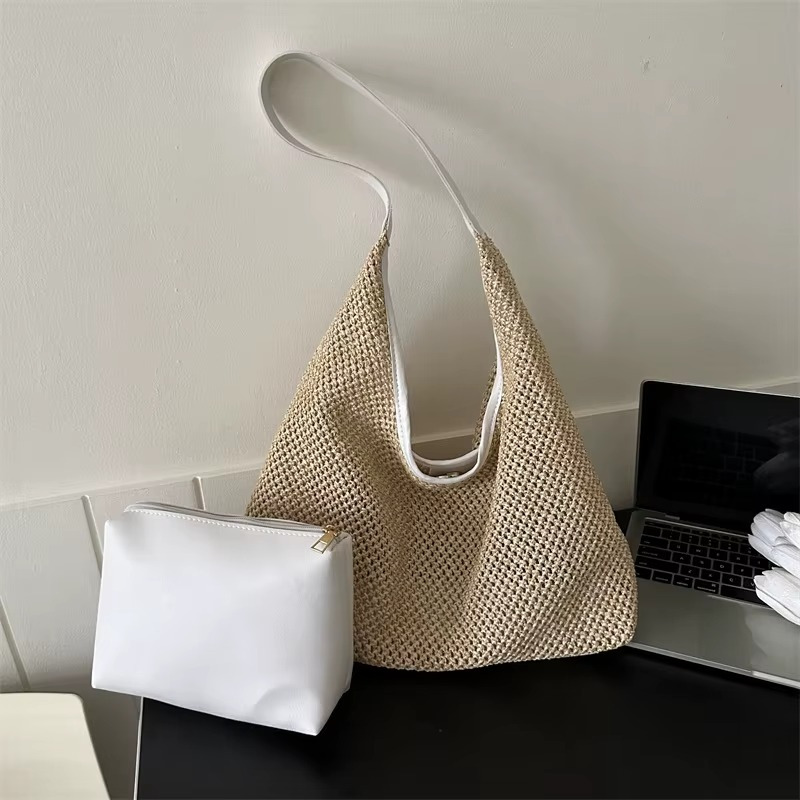 Sac en paille de plage tissée avec sangle fine blanche modèle Aurélie posé sur une table à côté d'une petite trousse blanche