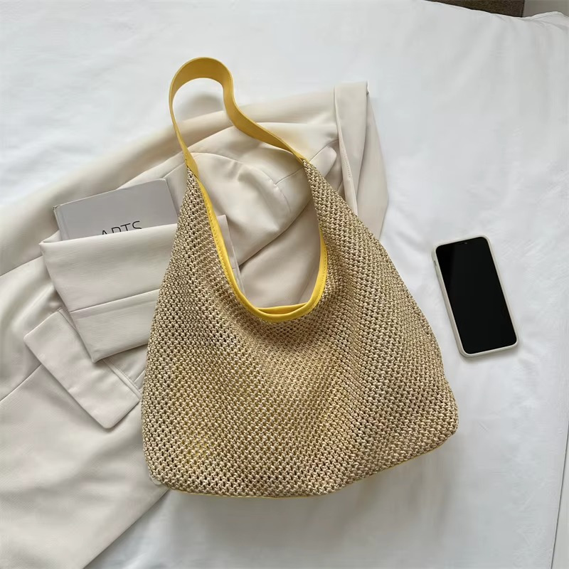 Sac en paille de plage tissée avec sangle fine jaune modèle Aurélie posé sur un vêtement clair