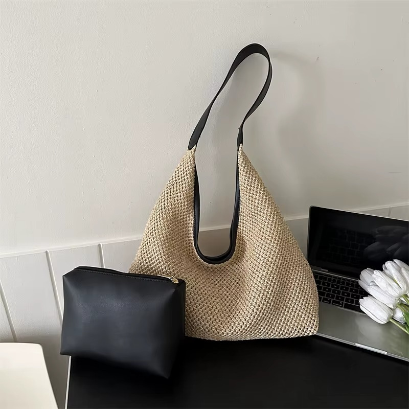 Sac en paille de plage tissée beige avec sangle fine noire et pochette noire posés sur une table près d'un ordinateur portable et des tulipes blanches