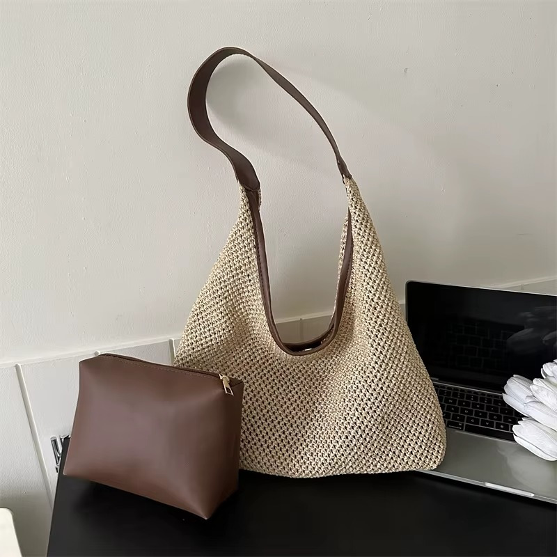 Sac en paille de plage tissée beige avec sangle fine marron et pochette marron posés sur une surface noire