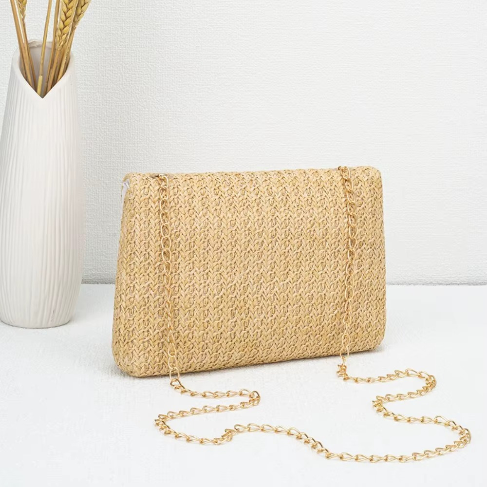 Sac en paille naturel avec rabat et fermoir chaîne dorée modèle Angélique posé sur une surface blanche à côté d'un vase blanc