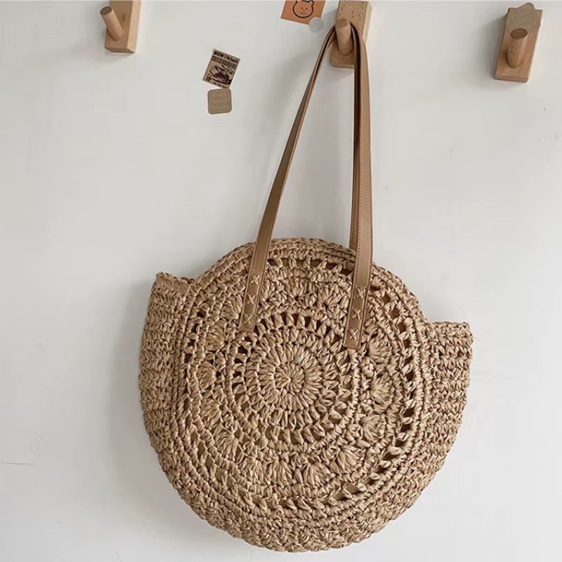 Sac En Paille Rond Ajouré Bandoulière – Solène Sac en paille rond ajouré avec bandoulière marron clair modèle Solène suspendu sur des crochets en bois