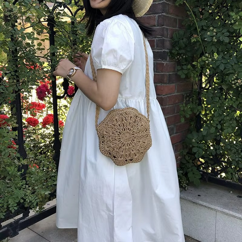 Sac en paille rond crochet dentelle plat couleur naturelle porté en bandoulière par une femme en robe blanche, vue de côté