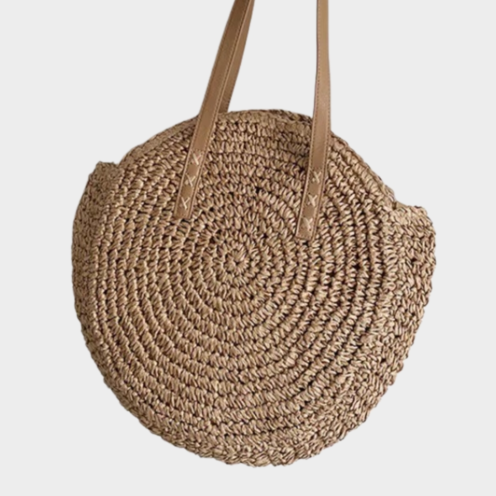 Sac En Paille Rond Tissage Uni Bandoulière – Adèle Sac en paille rond tissage uni couleur naturelle avec bandoulière en cuir modèle Adèle vu de face
