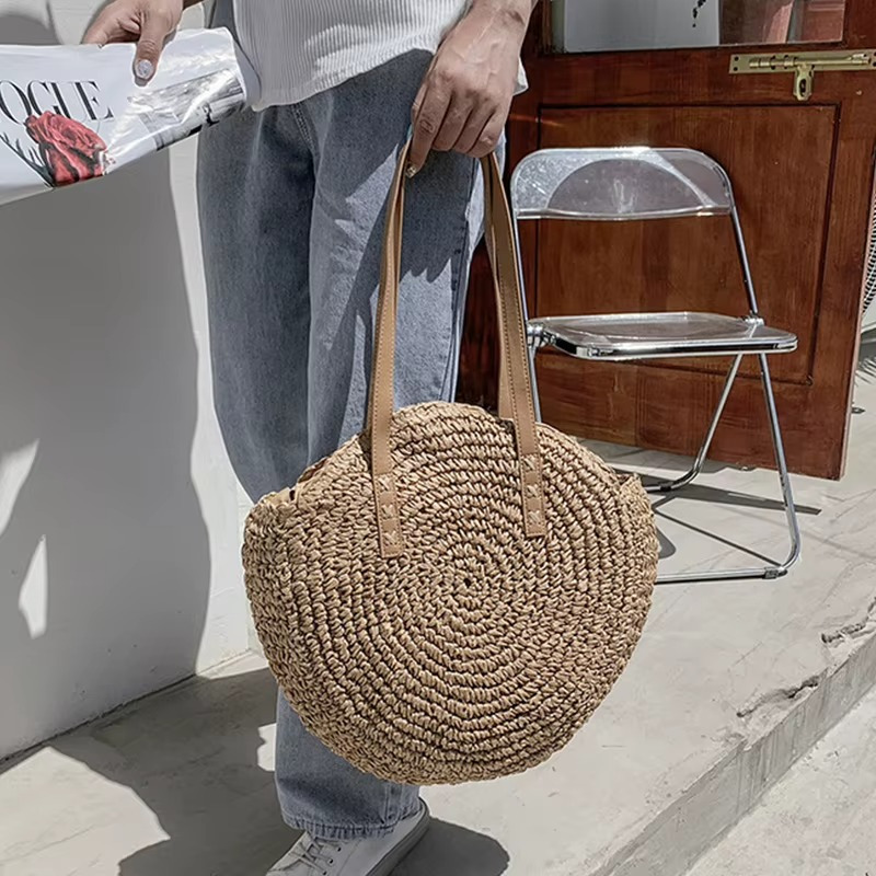 Sac En Paille Rond Tissage Uni Bandoulière – Adèle Sac en paille rond tissage uni avec bandoulière en cuir marron porté à la main