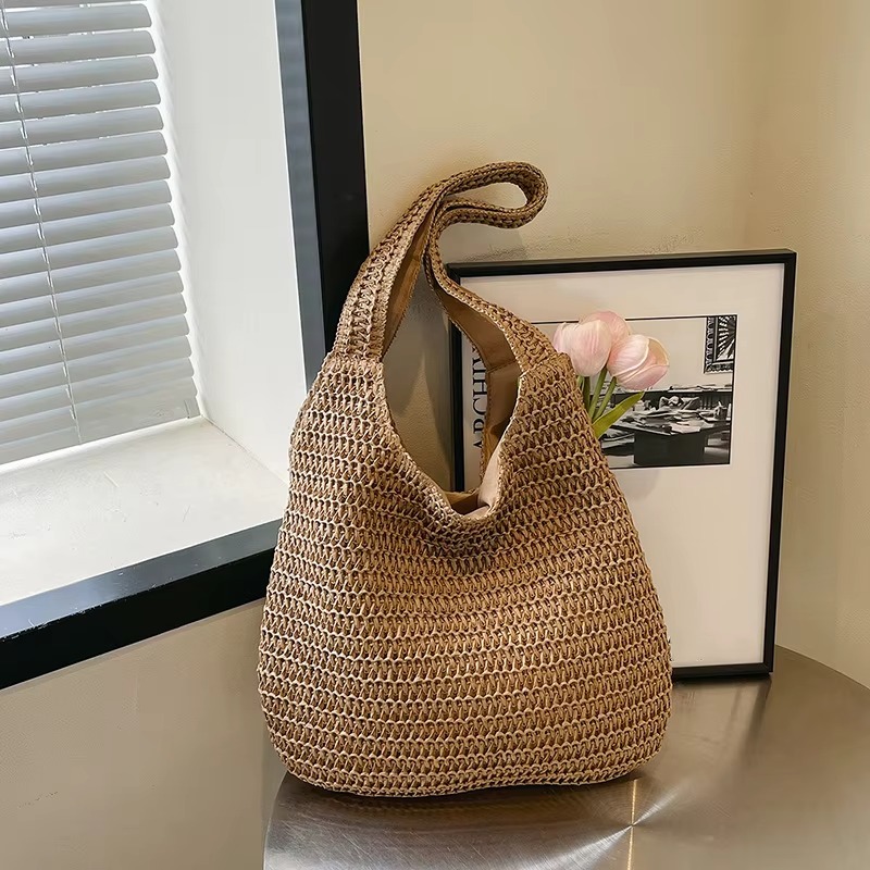 Sac En Paille Tissée Grande Capacité Double Anse – Camélia Sac en paille tissée grande capacité couleur naturelle avec double anse souple modèle Camélia posé sur une surface métallique devant un cadre photo