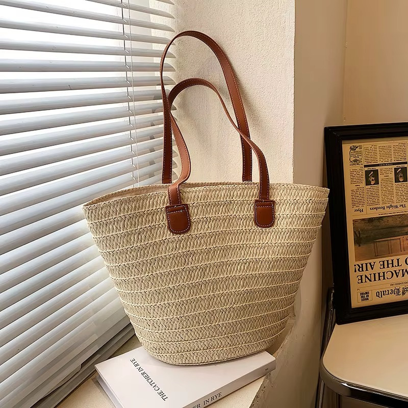 Sac en paille tressée bohème grande capacité Océane avec anses en cuir marron posé près d'une fenêtre