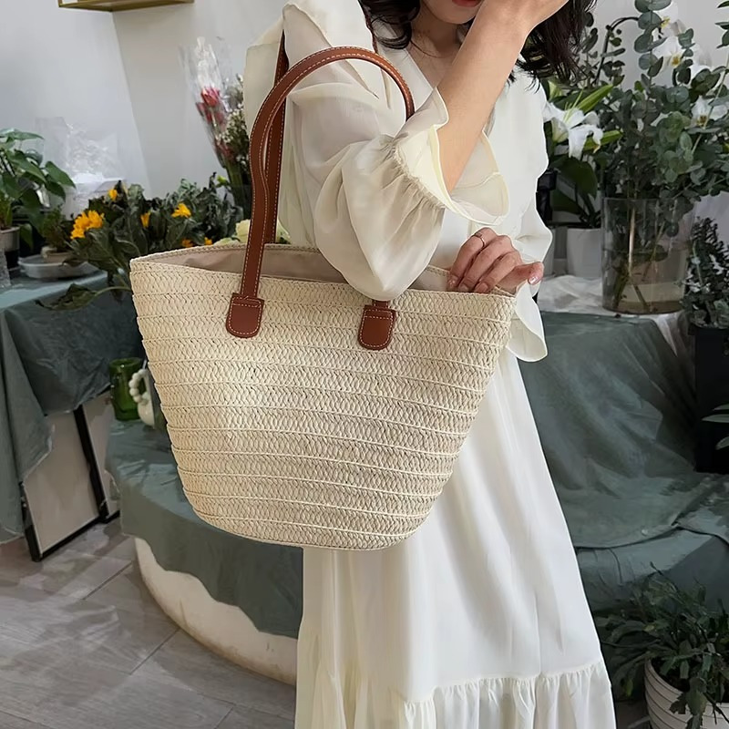 Sac en paille tressée bohème grande capacité couleur naturelle avec anses marron porté à l'épaule par une femme en robe blanche