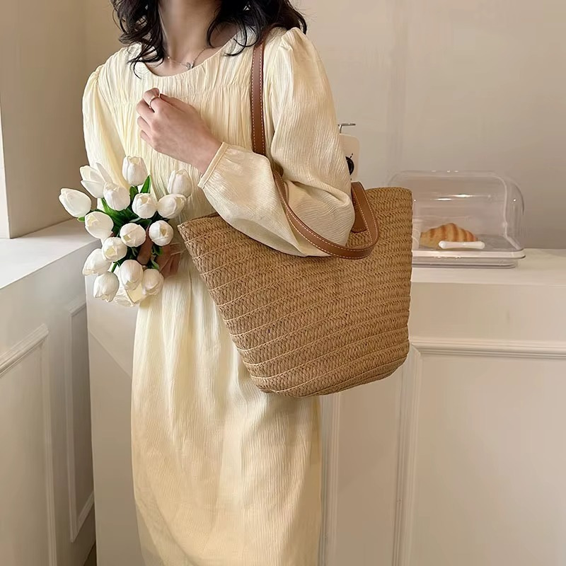 Sac en paille tressée bohème grande capacité modèle Océane porté à l'épaule par une femme en robe beige, forme arrondie avec anses marron