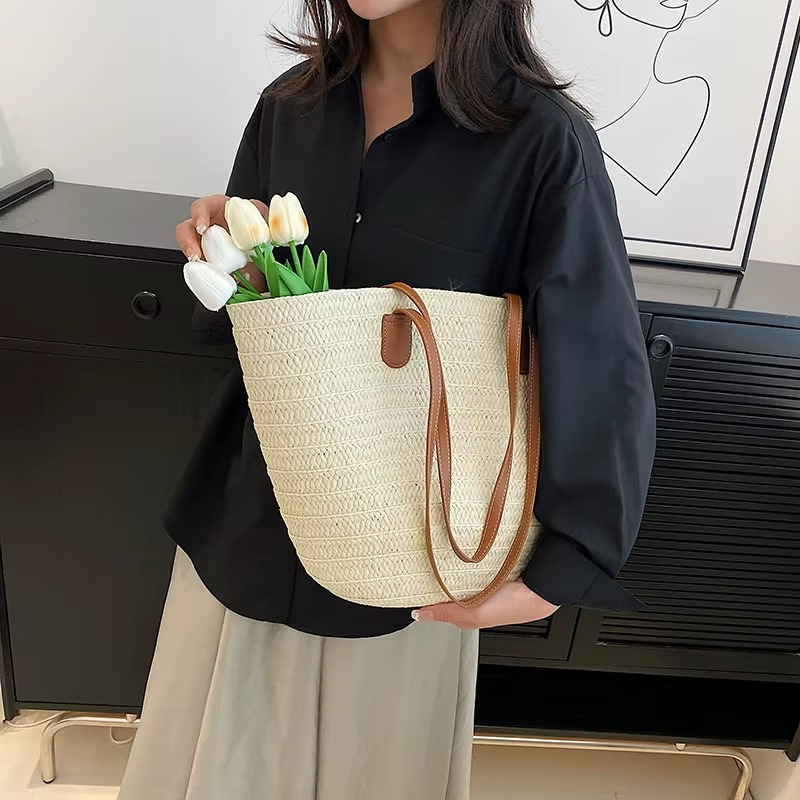 Sac en paille tressée bohème grande capacité Océane porté à l'épaule avec anses en cuir marron et bouquet de tulipes blanches à l'intérieur