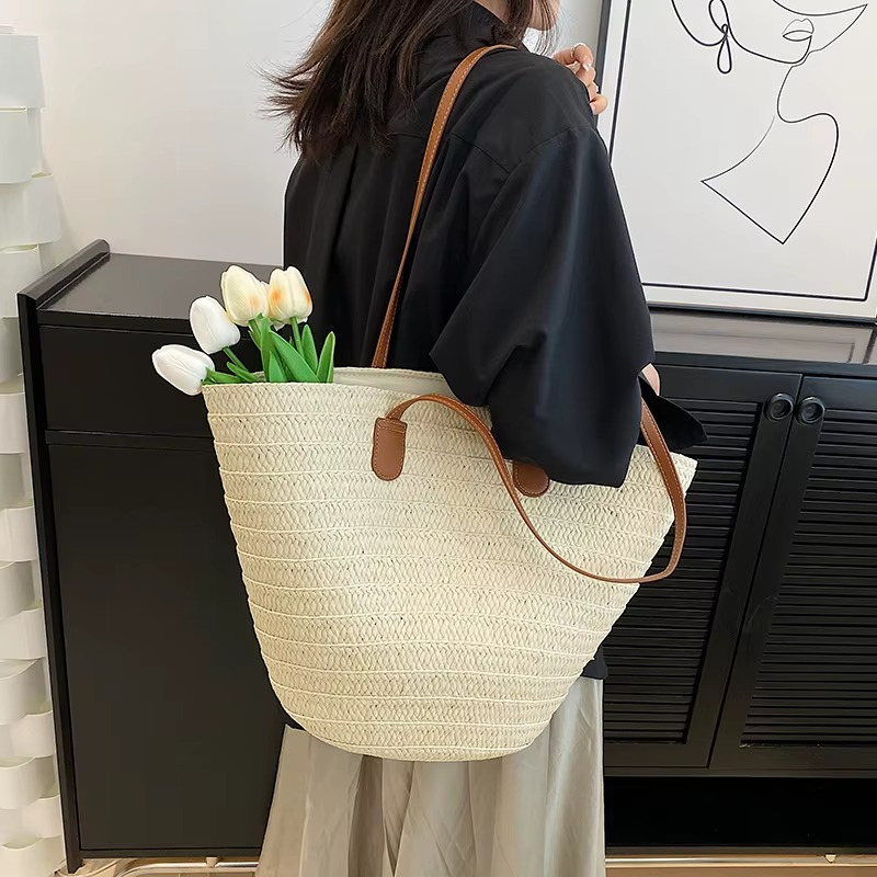 Sac en paille tressée bohème grande capacité Océane porté à l'épaule avec anses en cuir marron, contenant des tulipes blanches
