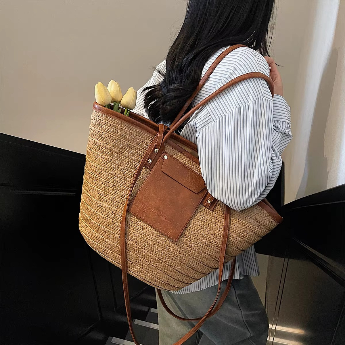 Sac en paille tressée cabas avec poche en cuir et rivets porté sur l'épaule, modèle Constance, détail de la poche en cuir marron