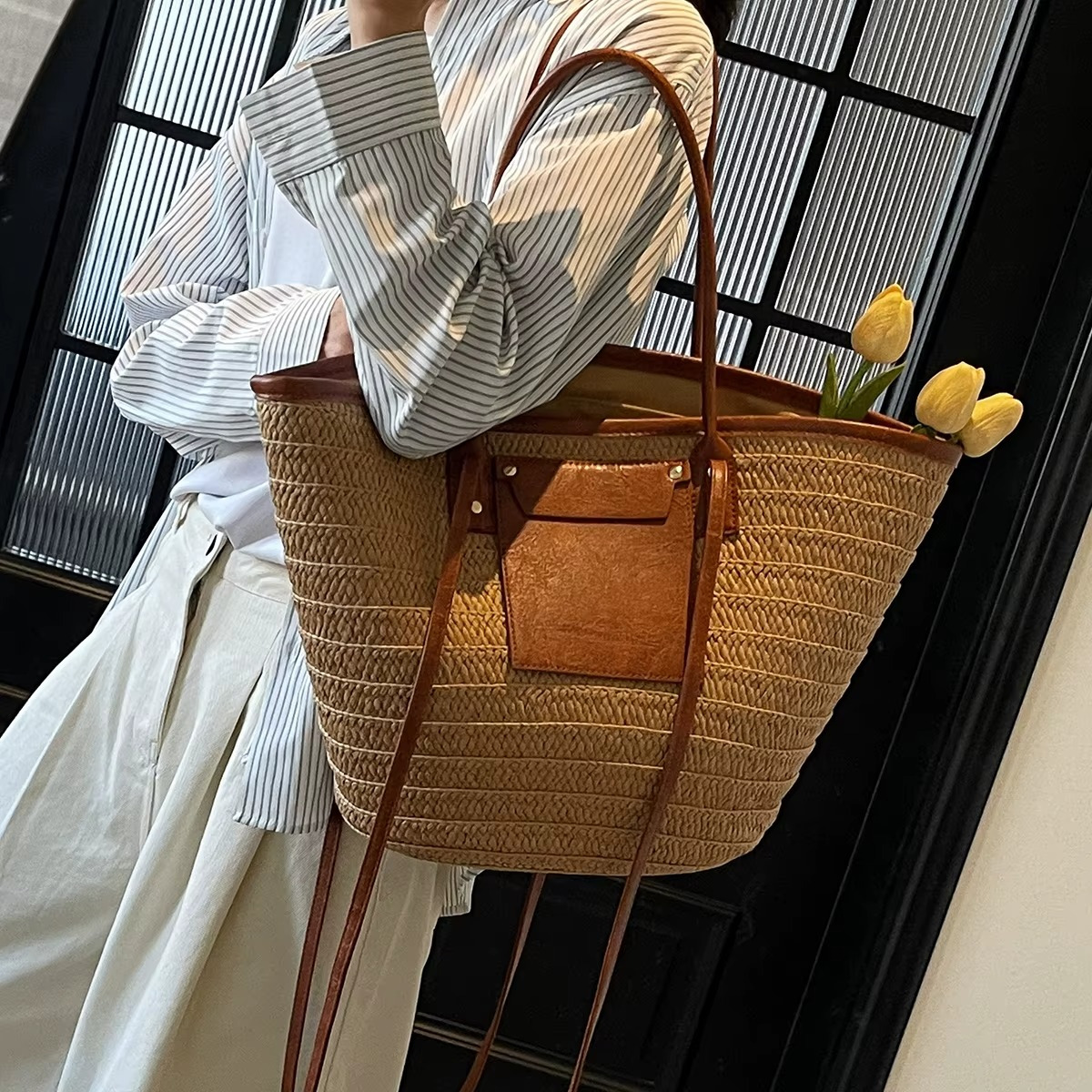Sac en paille tressée cabas avec poche en cuir marron et rivets porté à l'épaule