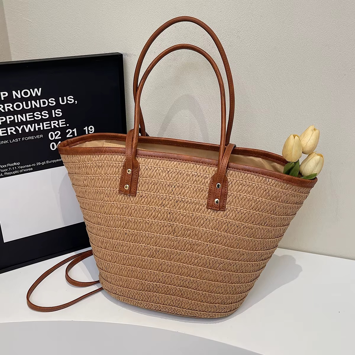 Sac en paille tressée cabas avec poignées en cuir marron et rivets, modèle Constance, vue de face avec tulipes jaunes à l'intérieur