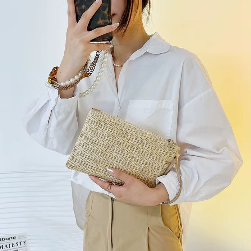 Sac En Paille Tressée Pochette Zippée Porte-Monnaie – Emma Sac en paille tressée pochette zippée beige porté à la main par une femme habillée en chemise blanche et pantalon beige