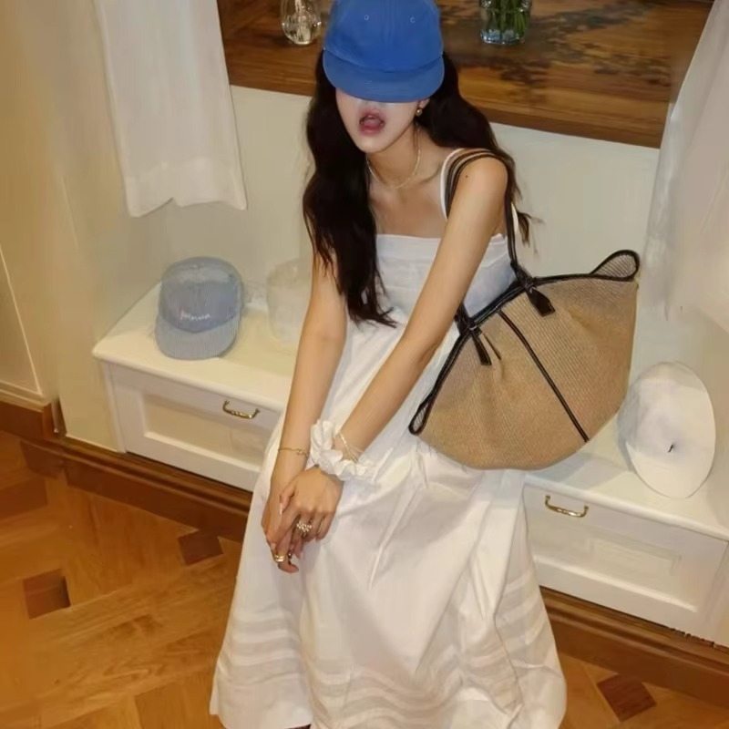 Sac en paille tressée seau avec liseré cuir noir porté à l'épaule par une femme en robe blanche et casquette bleue
