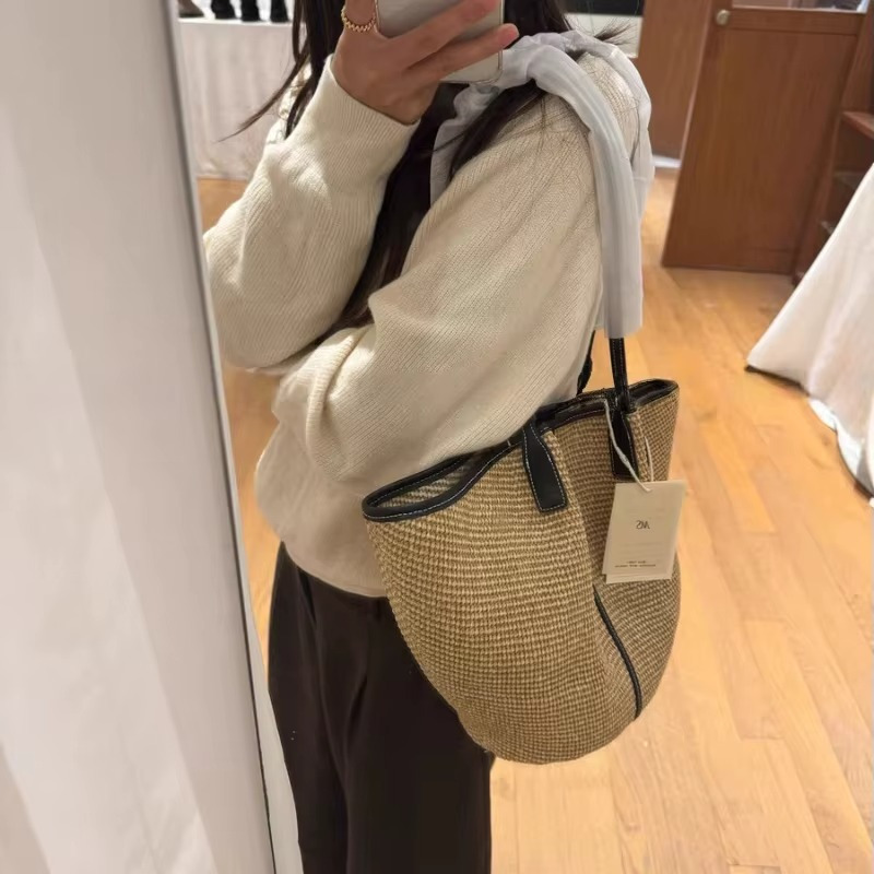 Sac en paille tressée seau avec liseré en cuir noir porté sur l'épaule, détail de la forme arrondie et anse fine