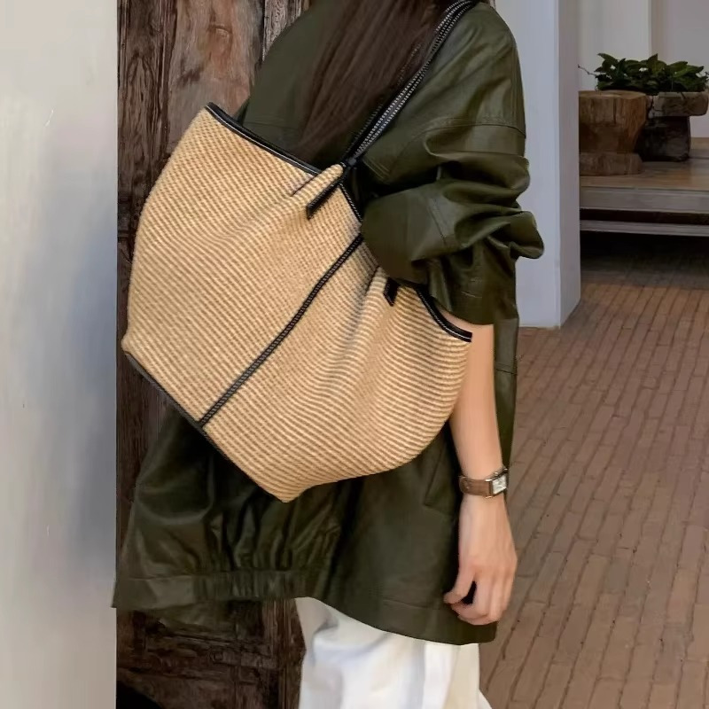 Sac en paille tressée seau avec liseré cuir noir porté sur l'épaule, vue de côté sur le détail des anses et la texture tressée