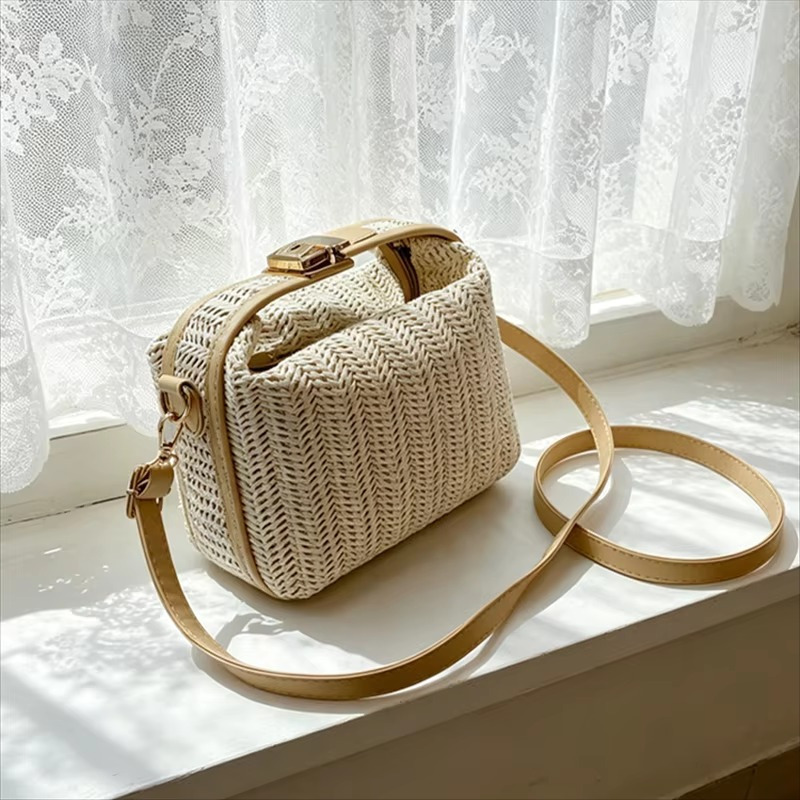 Sac en paille vintage rigide beige avec poignée et fermoir doré, bandoulière fine en cuir, posé sur un rebord de fenêtre devant un rideau blanc