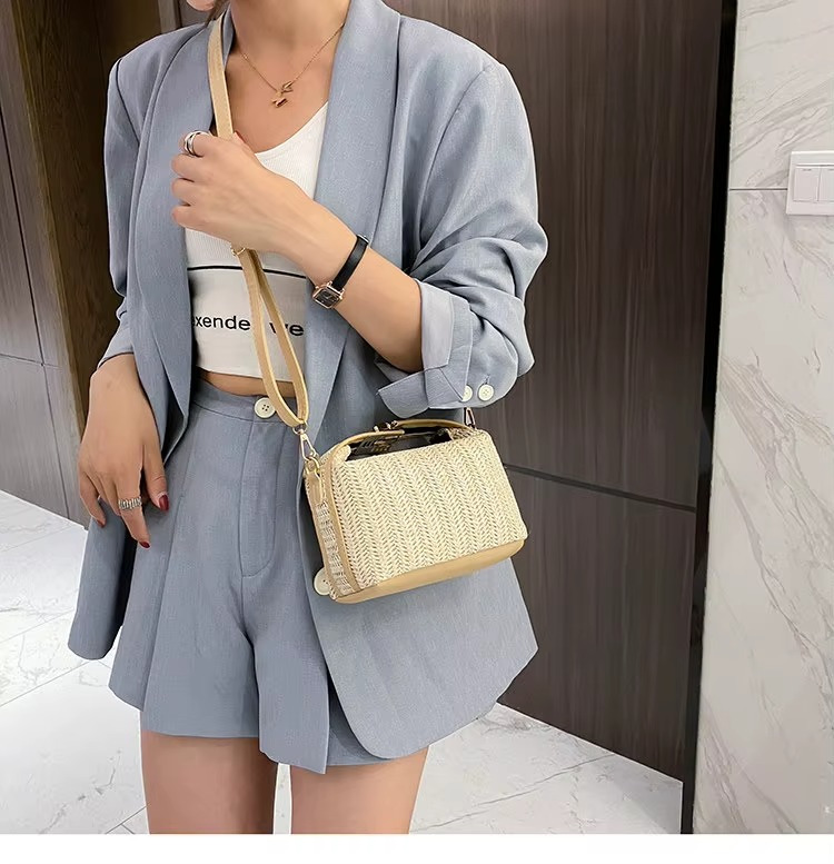 Sac en paille vintage rigide beige avec poignée fermoir doré et bandoulière fine porté en travers par une femme en tailleur gris