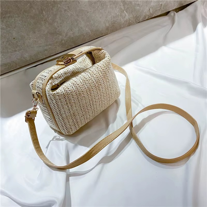 Sac en paille vintage rigide beige avec poignée et fermoir doré, bandoulière fine posée sur tissu blanc