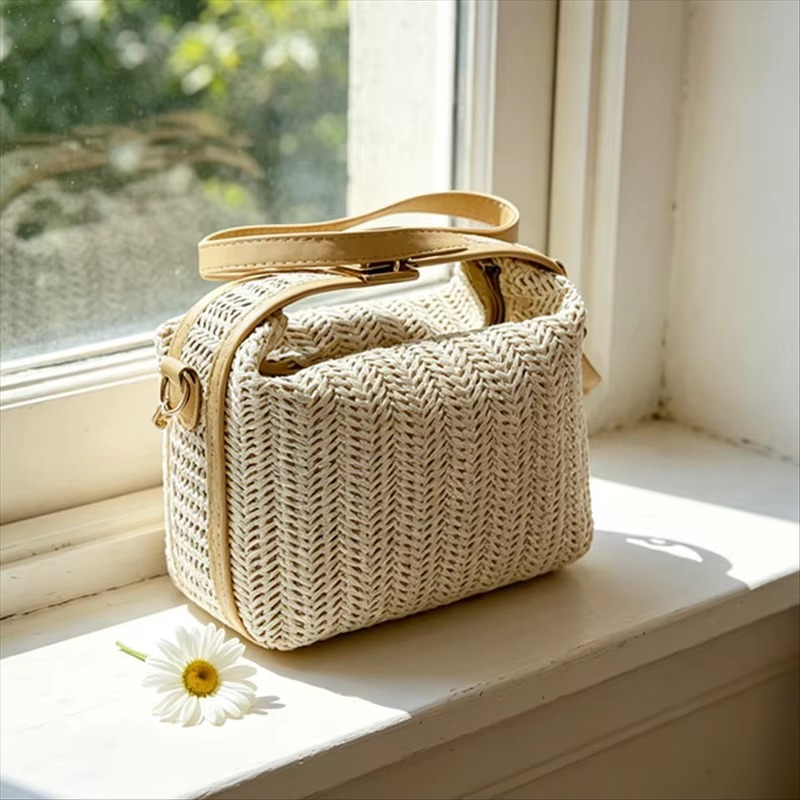Sac en paille vintage rigide beige avec poignée et fermoir doré, bandoulière fine, posé sur un rebord de fenêtre près d'une marguerite